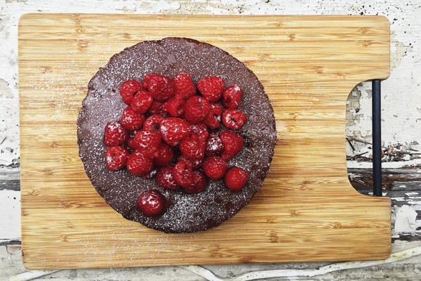 a whole chocolate zucchini cake on a wooden cutting board with raspberries on top