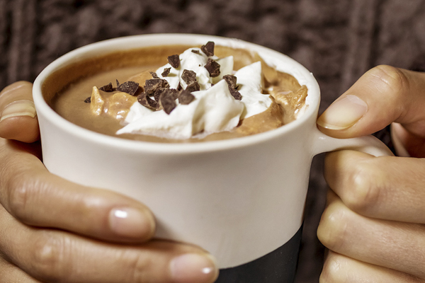 a woman's hands holding a mug of hot chocolate with whipped cream