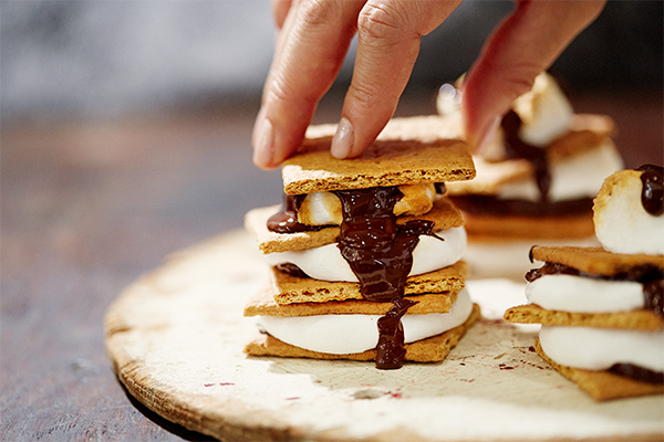 a hand pressing down s'mores so that the chocolate oozes out