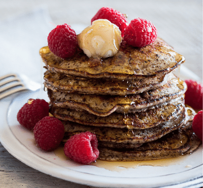 A stack of fluffy chocolate ricotta pancakes drizzled with maple syrup and topped with fresh fruit. The pancakes are served on a white plate.